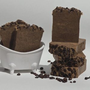 A Cafecito soap bar sits next to a bowl of coffee beans. This soap is likely scented like coffee.