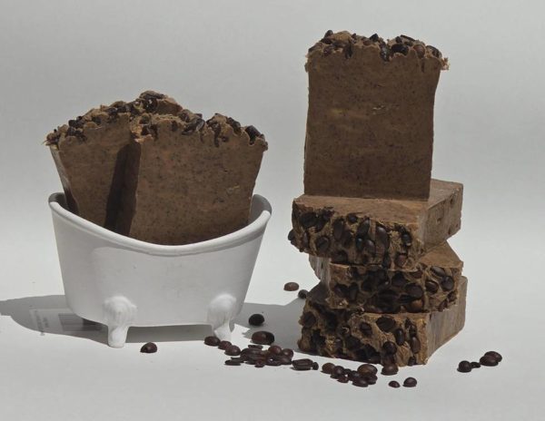 A Cafecito soap bar sits next to a bowl of coffee beans. This soap is likely scented like coffee.