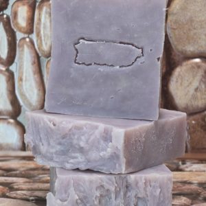 Three rustic bars of Lavender and Tallow soap are stacked on a stone-textured surface. The soap has a soft lavender hue with a slightly rough, handmade appearance. The top bar features an embossed outline, adding a unique touch to its natural look.