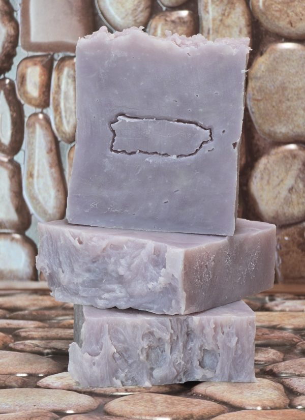 Three rustic bars of Lavender and Tallow soap are stacked on a stone-textured surface. The soap has a soft lavender hue with a slightly rough, handmade appearance. The top bar features an embossed outline, adding a unique touch to its natural look.